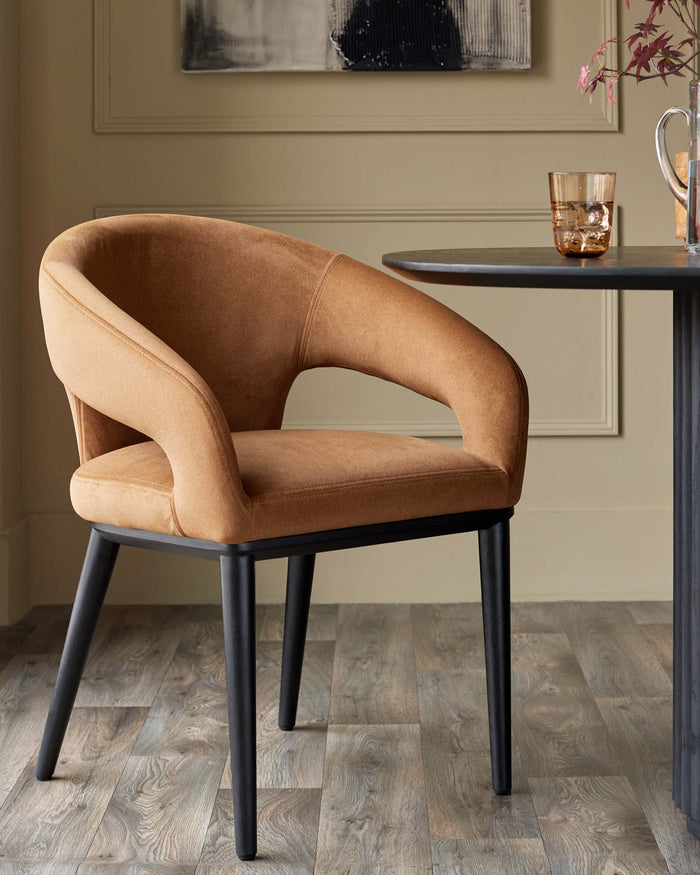 A caramel coloured chair with black legs sits next to a round table with a glass on it.