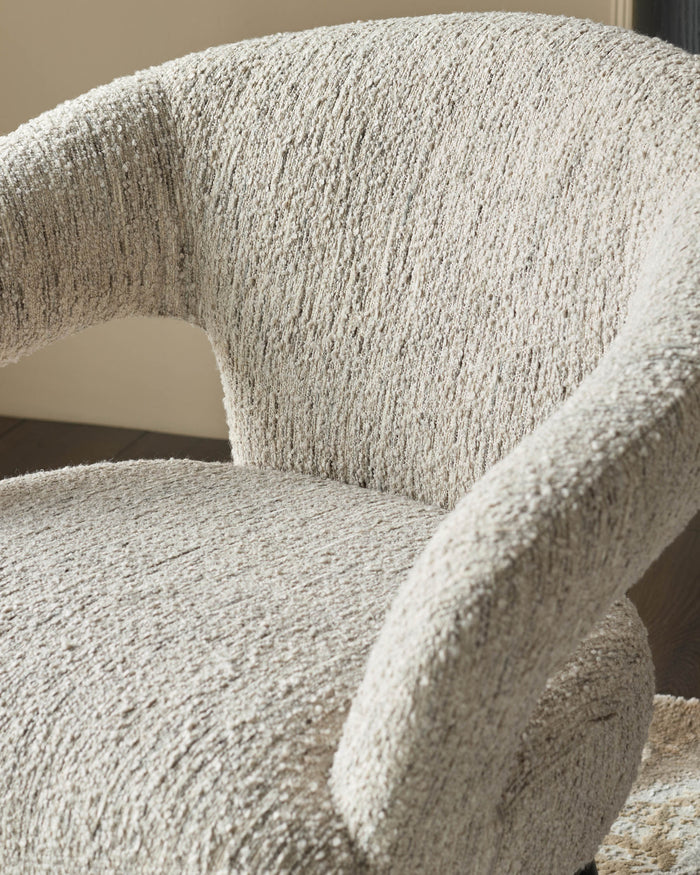 A close-up of a beige boucle armchair, showcasing its textured upholstery and curved design. Modern and inviting seating option.