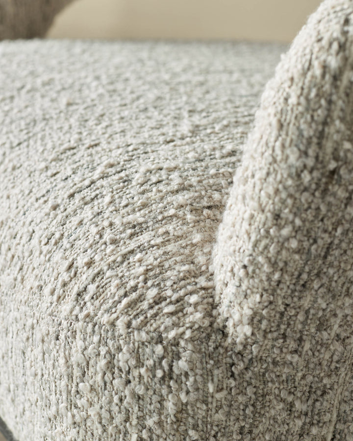 Close-up of a textured, light grey upholstered armchair, showing the detailed fabric and armrest.