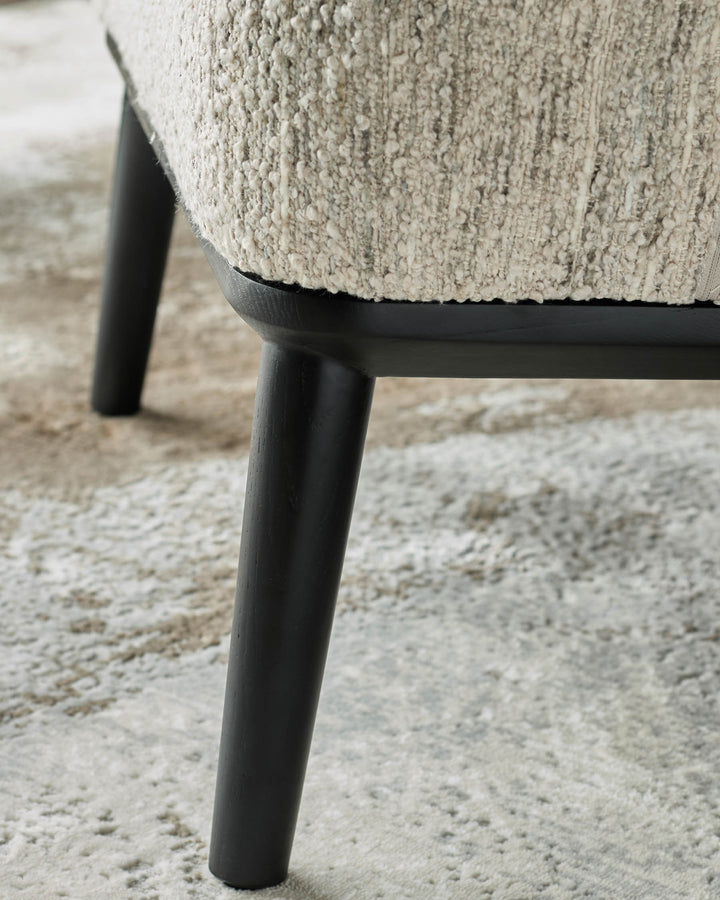 Close-up of a chair with textured upholstery and dark wooden legs, showcasing its design and quality materials.