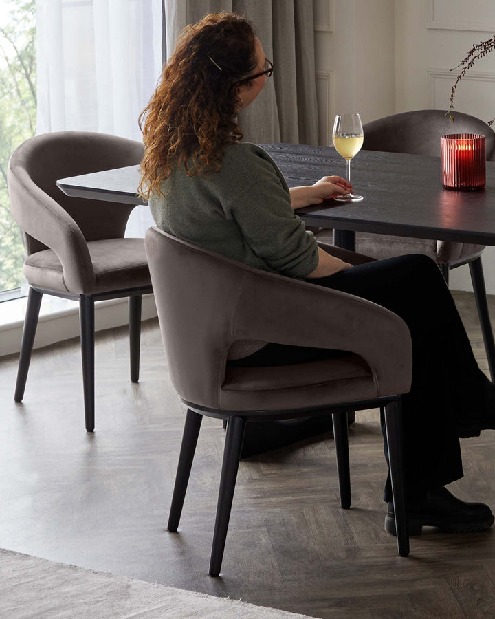Elegant modern dining set with a textured dark wood round table and plush upholstered dining chairs in a soft grey fabric with a smooth curved design and black legs.