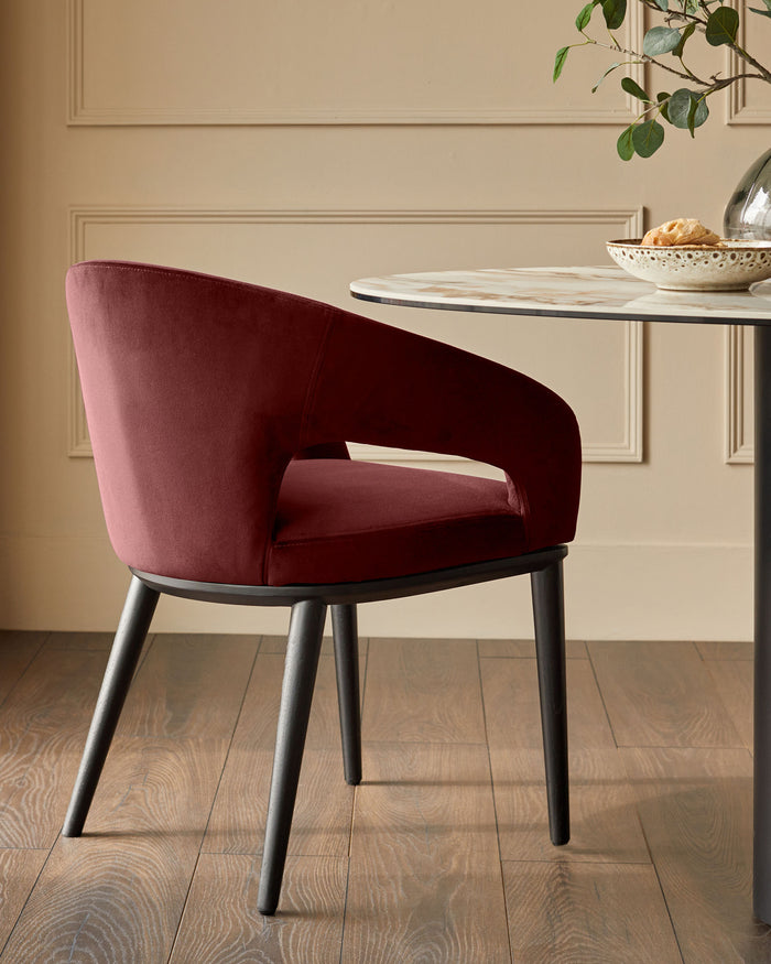 Maroon velvet dining chair with black legs at a round marble table, exuding modern elegance.