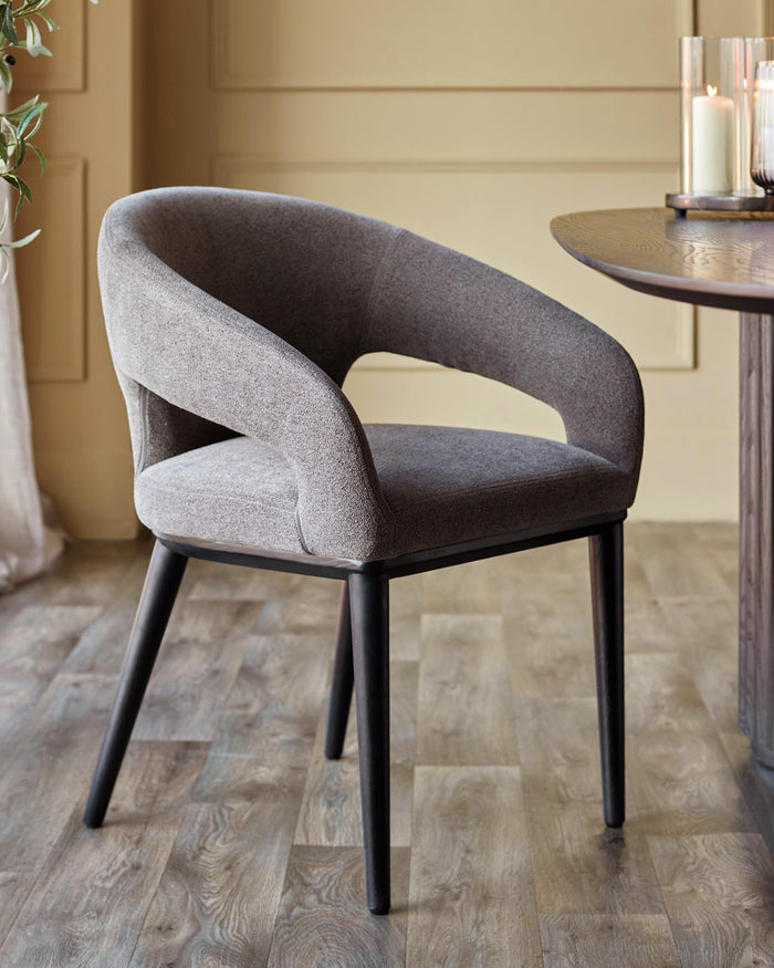 A stylish, grey upholstered dining chair with black legs, positioned near a wooden table, enhancing a modern dining space.