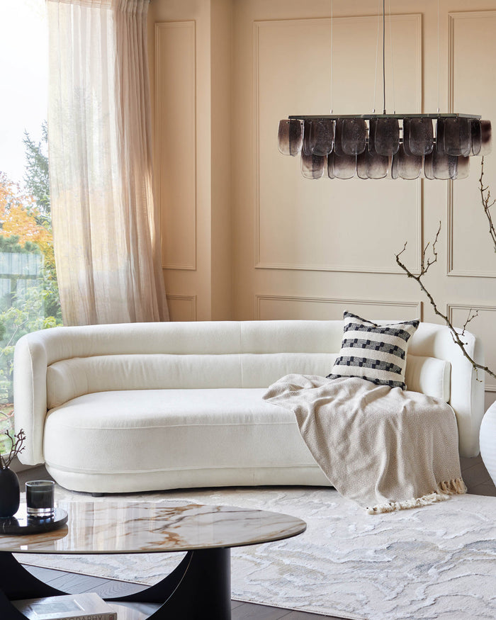 Stylish living room featuring a modern white sofa, marble coffee table, patterned rug and unique pendant light.