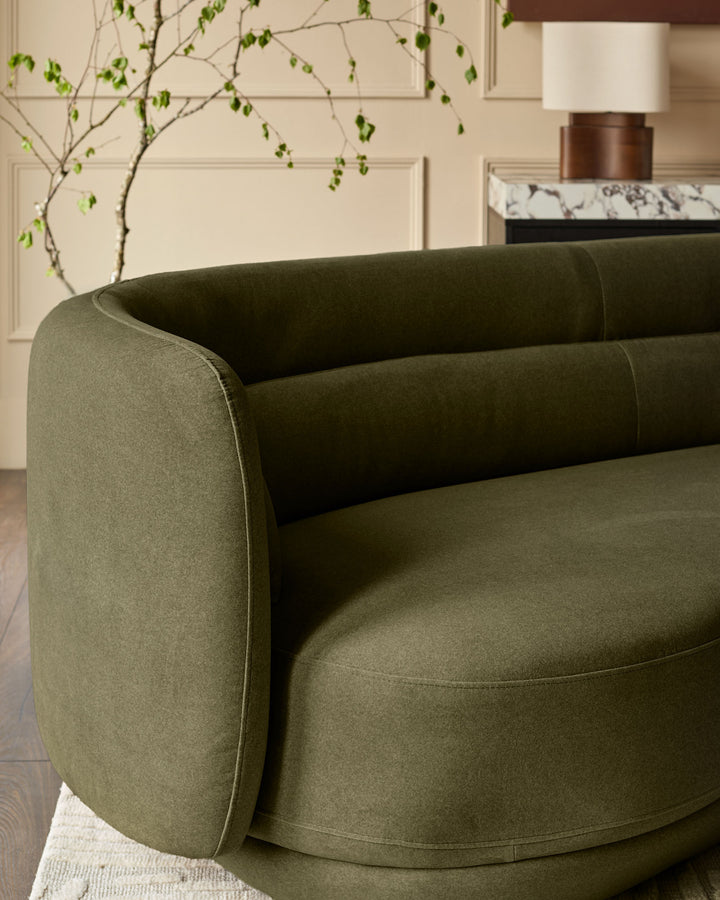 Henry 3-seater sofa in olive green velvet with curved arms, shown from angled side view in a styled living room setting.