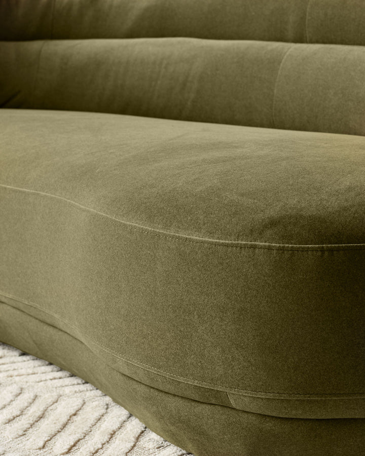 Close-up of Henry 3-seater sofa in olive green velvet, showing curved arm detail and seating surface with visible stitching.