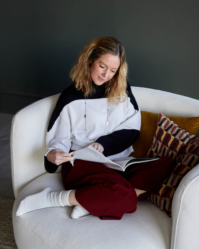 An armchair with a woman reading a magazine. The armchair is off-white and has cushions.