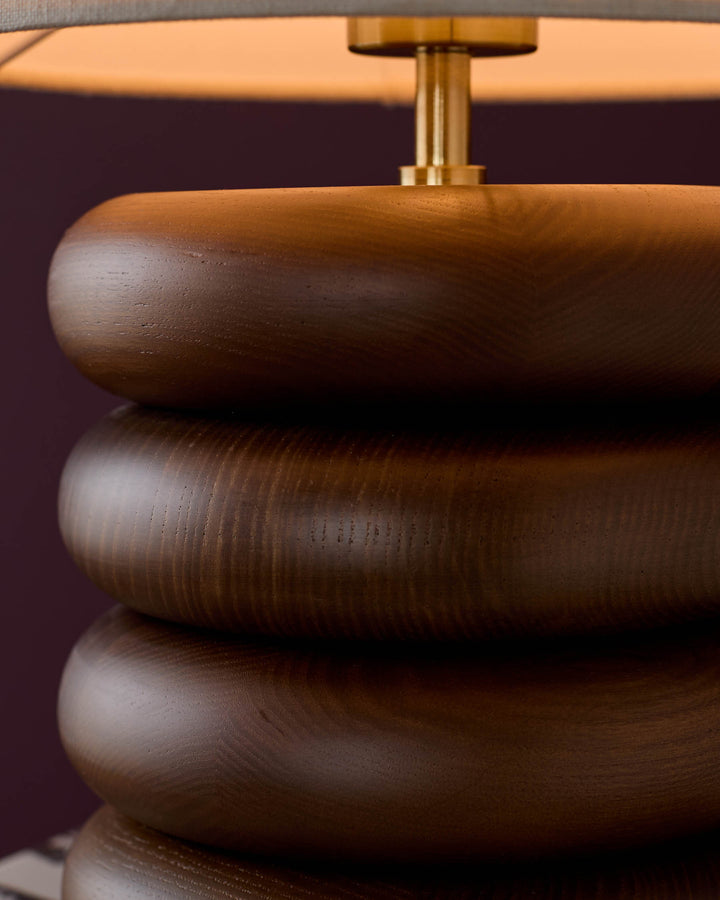 Dark wood table lamp with stacked cylindrical base and brass fixture, linen shade visible at top.