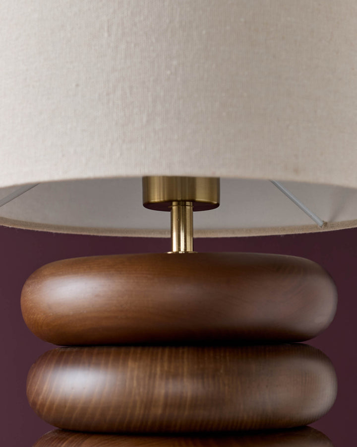 Hepworth table lamp with stacked dark wood base, brass connector, and natural linen shade, front view.