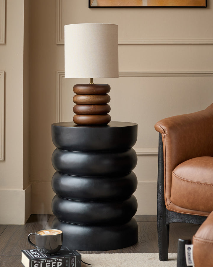 Black stacked side table with mango wood lamp base in contemporary living room setting.