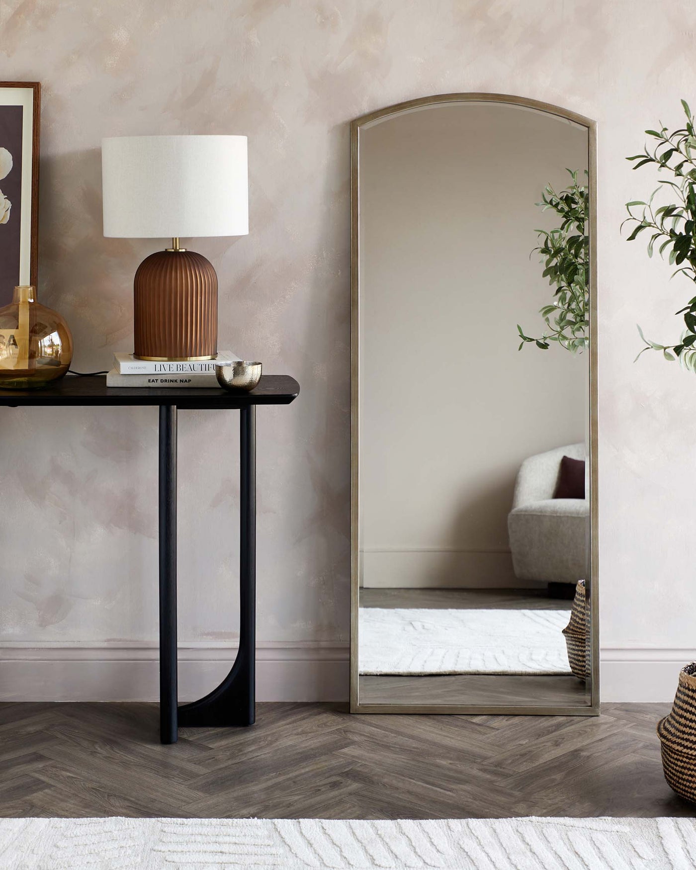 Elegant black console table with a straight front, narrow rectangular shape, and two vertical support legs at one end, complemented by a modern, oversized arch-top floor mirror with a minimalistic metallic frame.