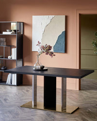 Modern black dining table with gold base, stylish vase, and decorative bowl. Background features a minimalist shelving unit.