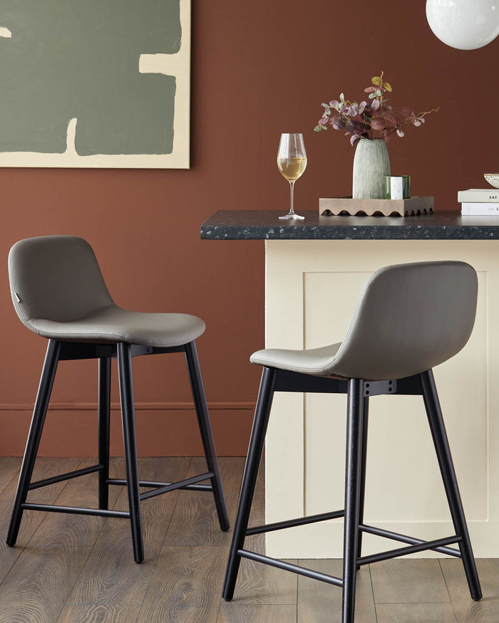 Two grey bar stools with black legs are positioned in front of a counter for a stylish kitchen or bar setting.