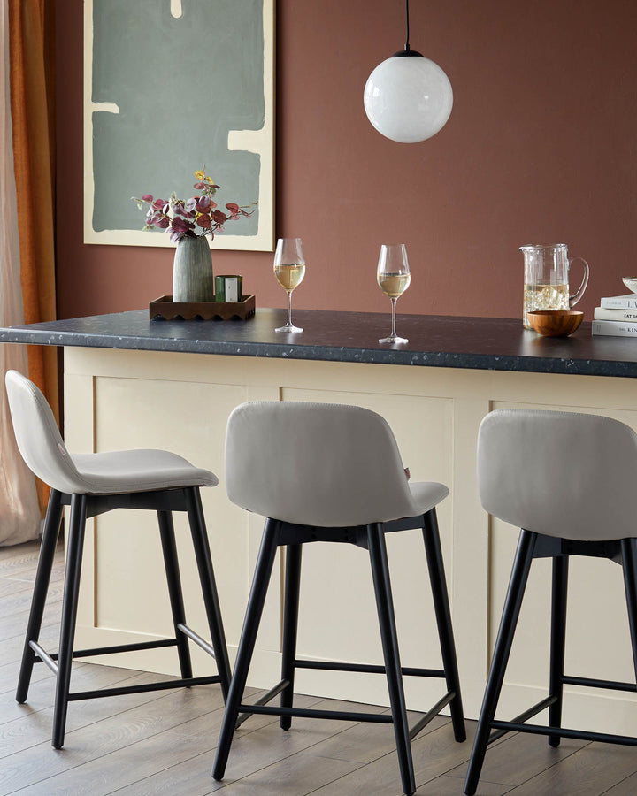 Three modern bar stools with grey seats and black legs at a kitchen island.