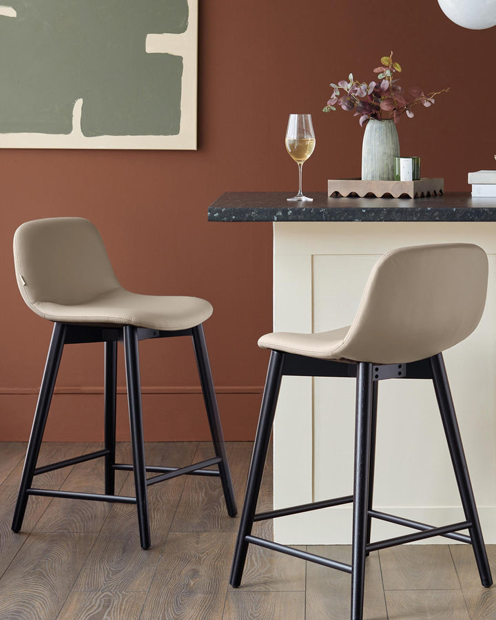 Two stylish bar stools with black legs and taupe seats are positioned beside a kitchen island.