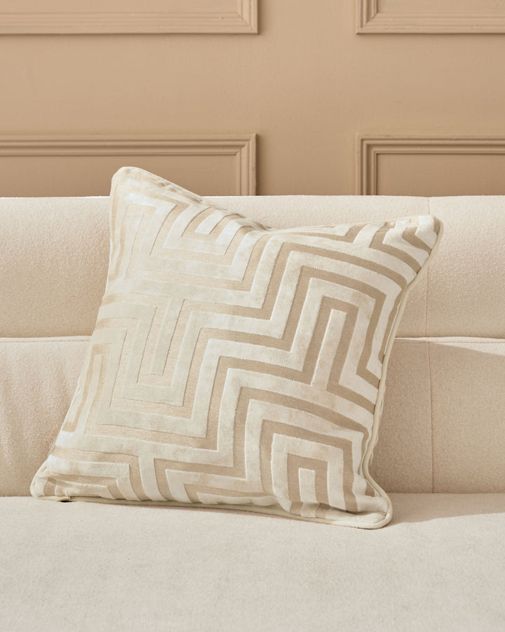 Imani cushion in ivory with geometric tan and cream striped pattern, displayed on a beige upholstered sofa.