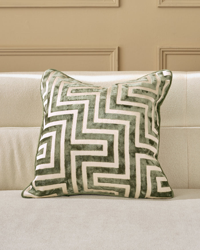 Imani cushion in medium olive green with cream geometric pattern, displayed on a beige sofa.