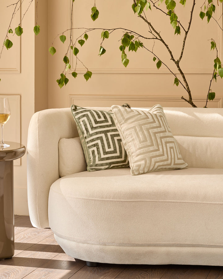 Imani Cushion in Medium Ivory with geometric pattern, displayed on cream curved sofa in modern living room setting.