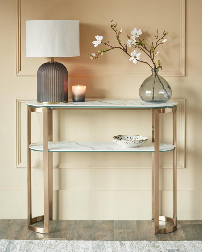 Console table with marble shelves and a gold frame, decorated with a lamp, vase, candle and bowl.