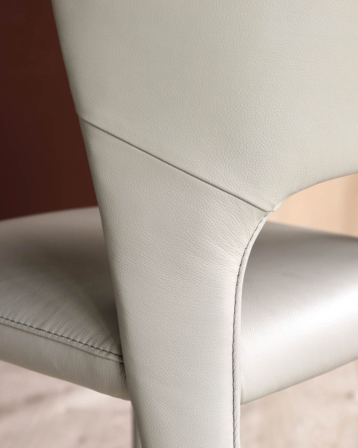 Jackson dining chair in light grey leather, close-up of curved backrest and seam detail.