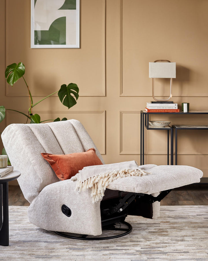A recliner chair with a throw and cushion, next to a side table, with artwork and a side table visible in the background.