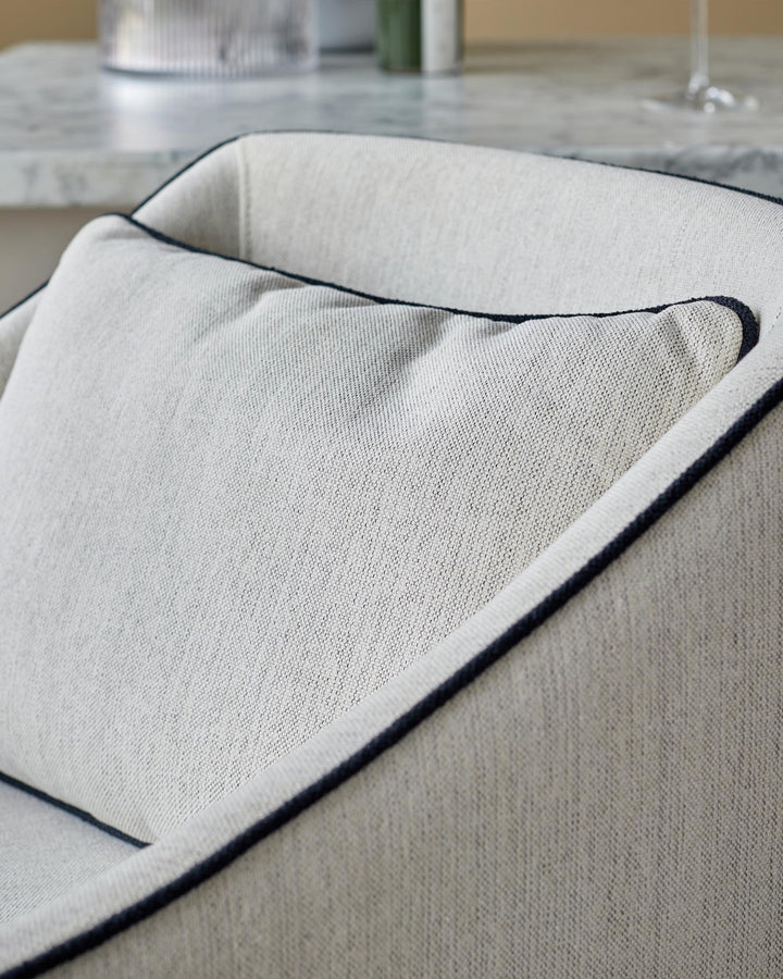 Close-up of a cream armchair with a piped cushion, exuding comfort and understated elegance.