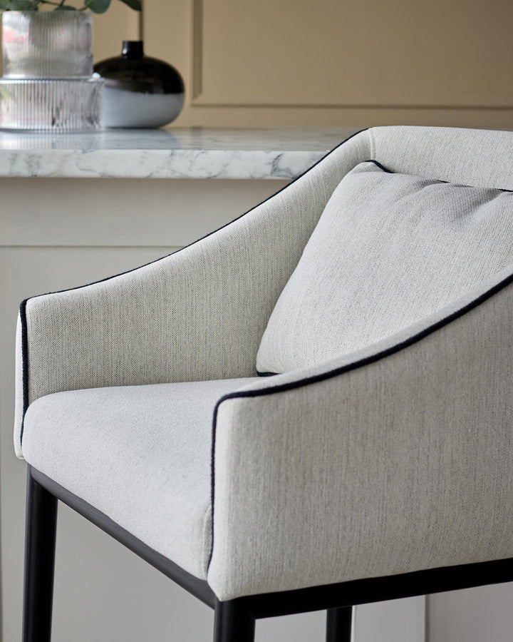 A light-grey upholstered arm chair with black trim and dark legs, positioned in front of a kitchen island.