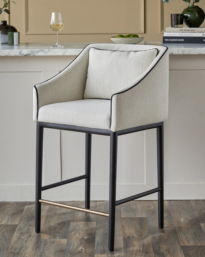 An arm chair bar stool with a cream upholstered seat and a black metal frame. A stylish addition to any kitchen or bar area.