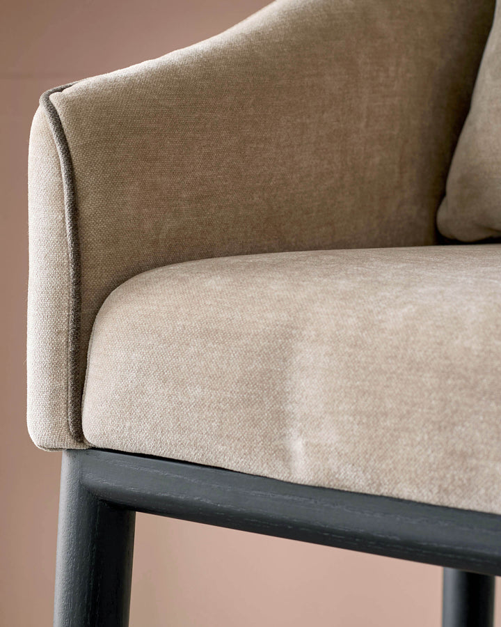 Champagne fabric bar stool with curved backrest and dark wooden legs, shown in close-up detail.