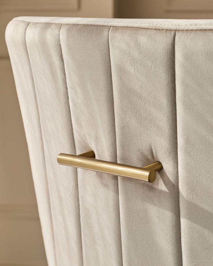 Champagne velvet dining chair with pleated backrest and brass handle detail, close-up view.