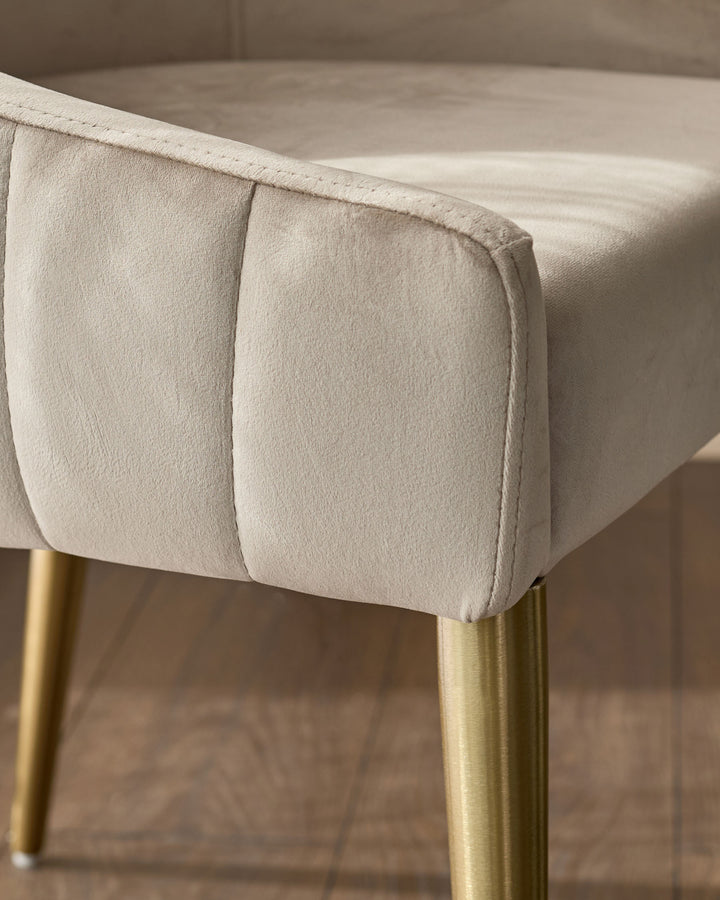 Champagne velvet dining chair with pleated seat detail and brushed brass legs, close-up side view.