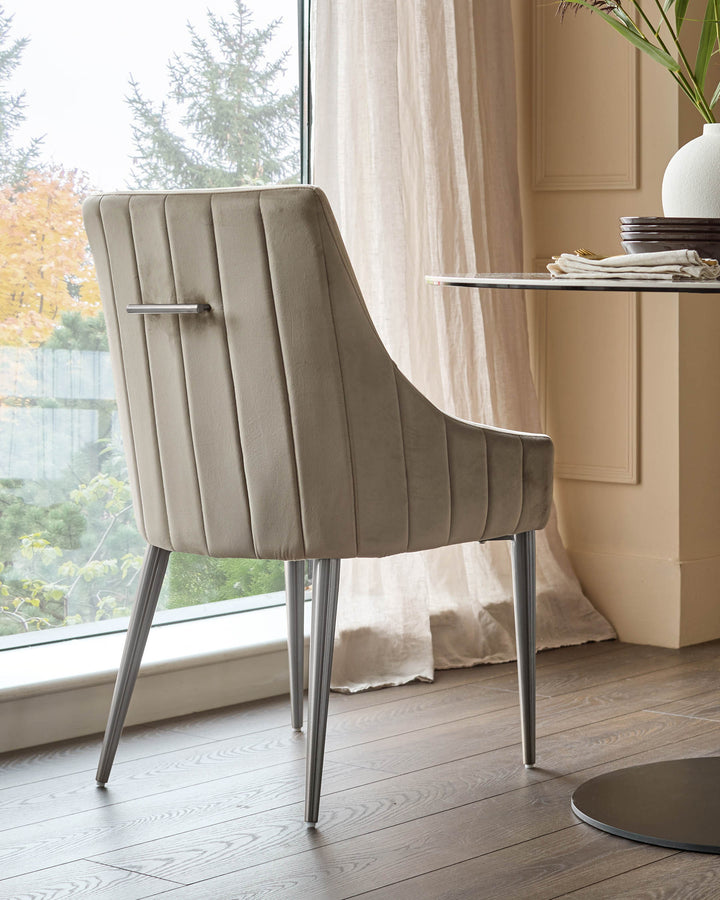 Champagne velvet dining chair with vertical channel tufting, stainless steel legs, and arms, shown in bright interior setting.