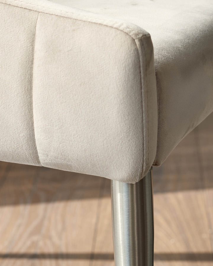 Champagne velvet dining chair with curved backrest and brushed stainless steel leg, detail view.