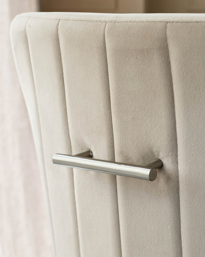 Champagne velvet dining chair with vertical channel stitching and brushed stainless steel handle detail.