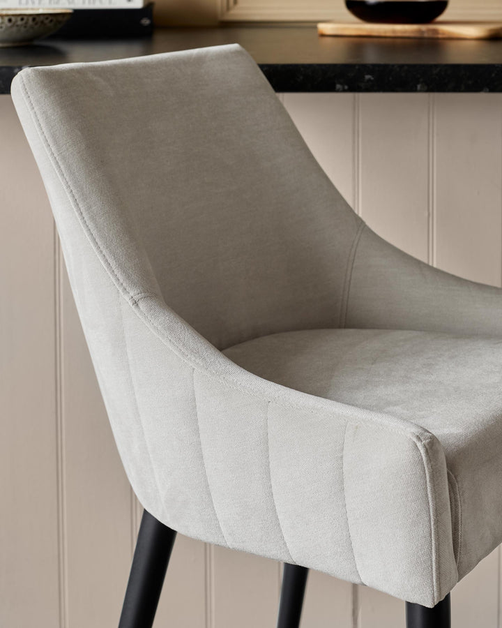 Close-up of a stylish, light grey upholstered chair with black legs, set against a neutral background.