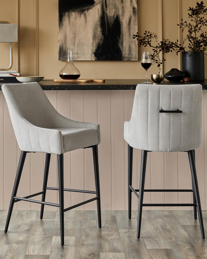 Two stylish, modern bar stools with grey upholstery and black metal legs sit in front of a bar.