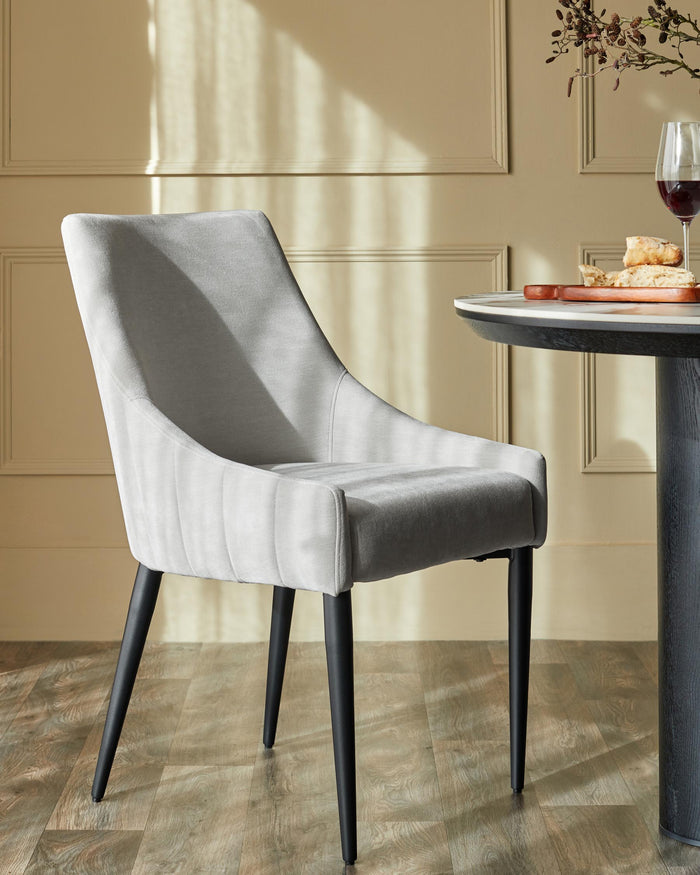 Upholstered dining chair with black legs next to a dining table with food and drink.