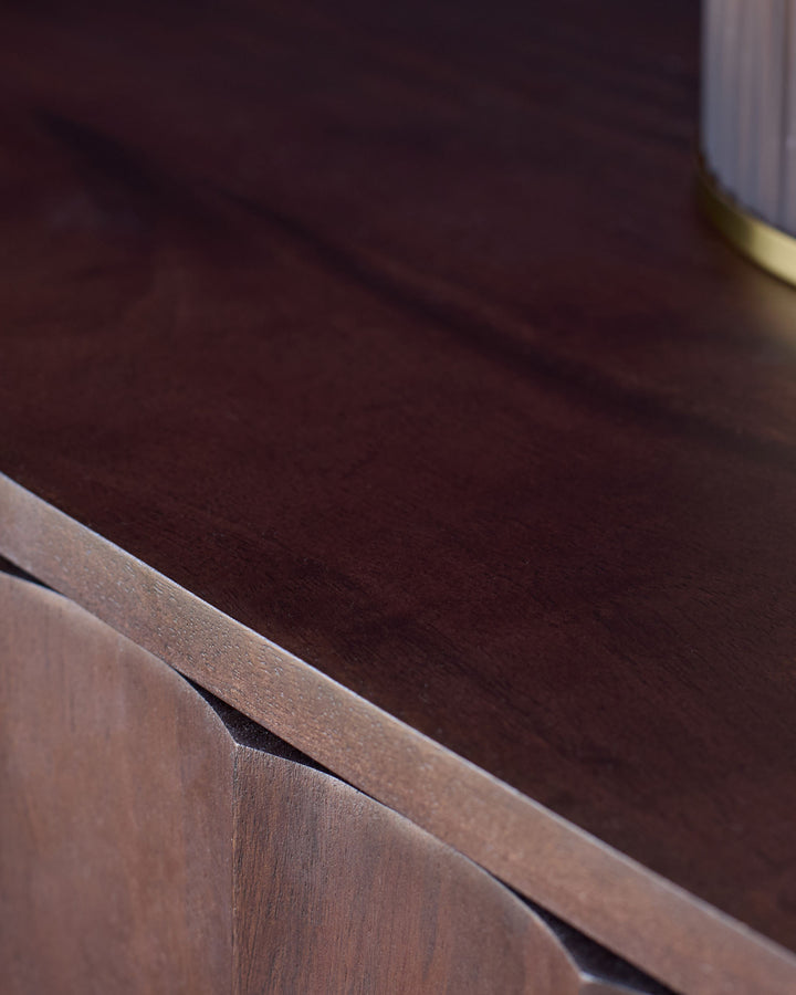 Dark mango wood bedside table with natural grain finish and curved edge detail, angled close-up view.
