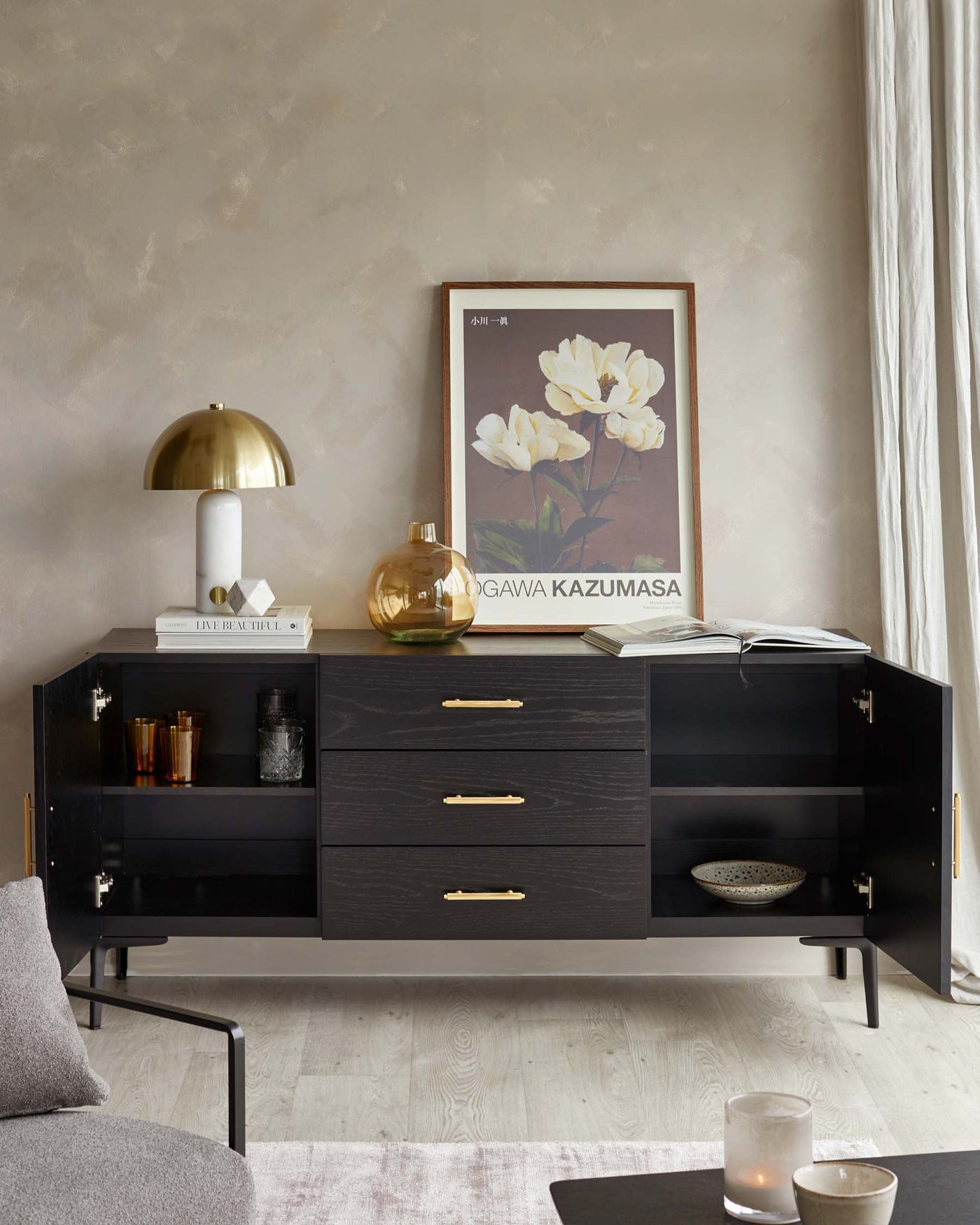 Modern black wooden sideboard with gold handles, featuring two closed cabinets and three drawers, styled with decorative items on top, against a textured wall.