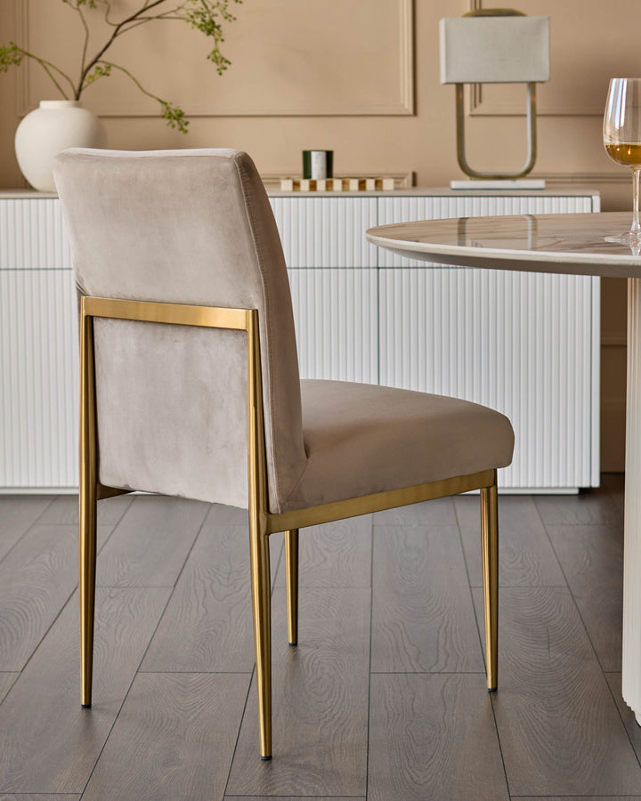 Keira velvet dining chair in champagne with gold metal legs, shown from a side angle in a modern dining room setting.