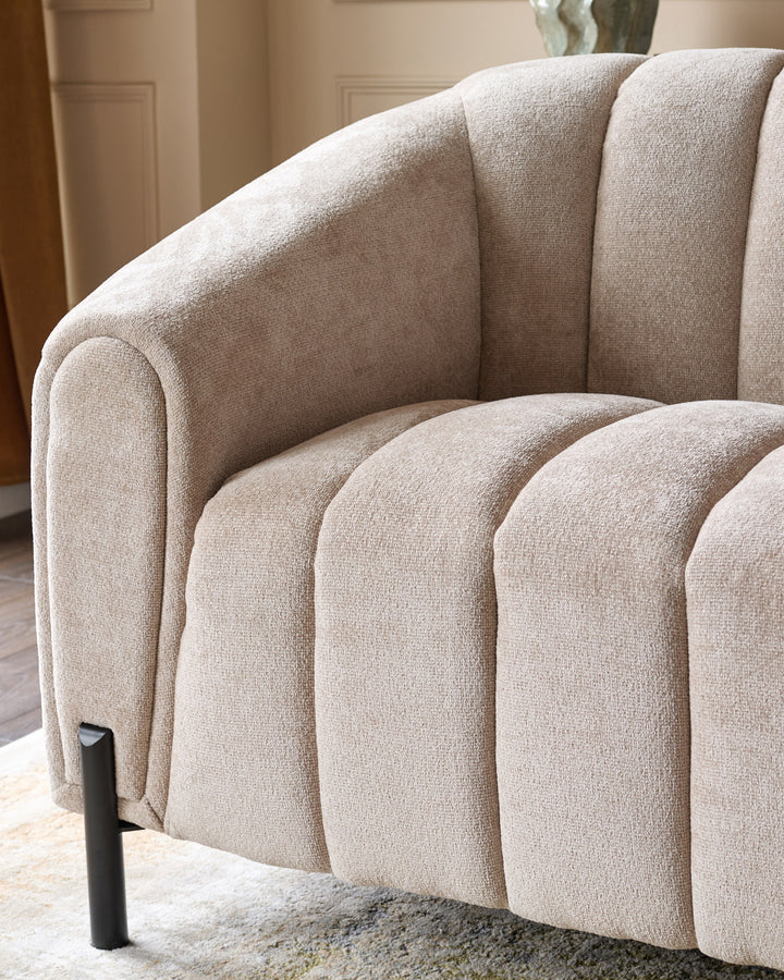 Kendra 3-seater sofa in natural fabric, showing curved channel-quilted design and rounded armrest from side angle.