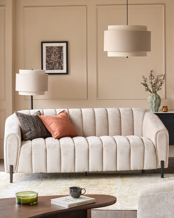 Kendra 3-seater sofa in natural fabric with vertical channel quilting, curved arms, and black metal legs in a modern living room setting.