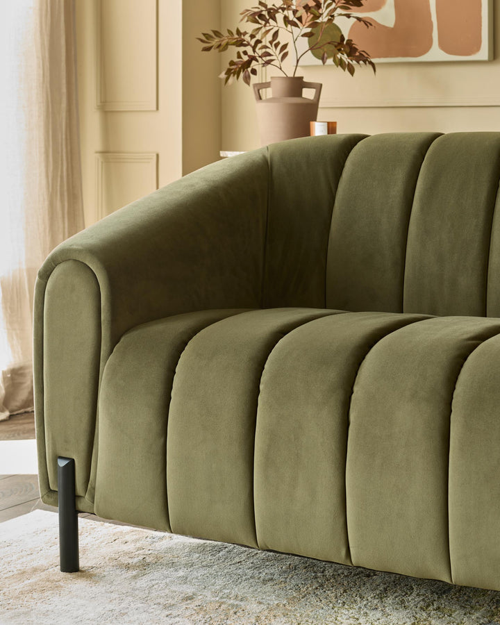 Close-up of an olive green, channel-back sofa with sleek black legs in a stylish living room setting.