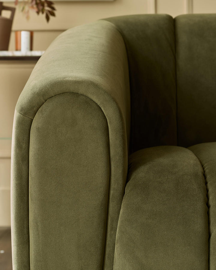 Close-up of an olive green velvet armchair, showing the curved arm and plush texture. A luxurious seating option.