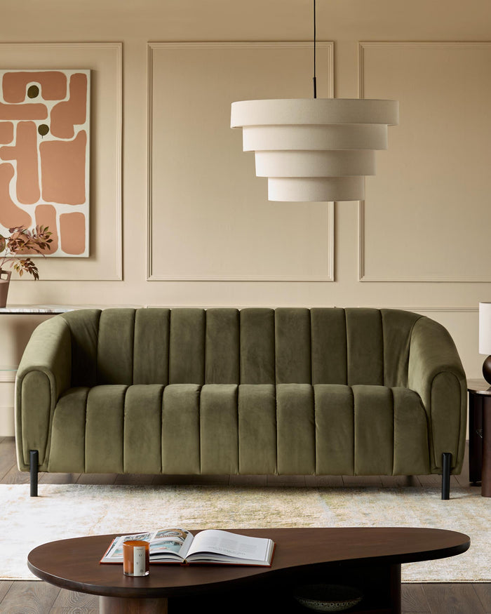 Olive green sofa, with a unique coffee table, on a patterned rug. A statement lamp hangs above in a neutral room.