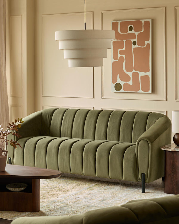 A stylish living room featuring a green velvet sofa, a layered lampshade and modern art.
