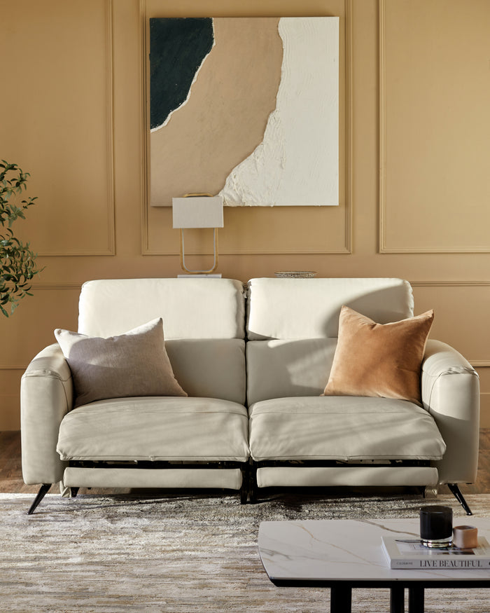 A modern cream leather sofa with cushions, positioned in front of abstract art and a stylish, neutral coloured rug.