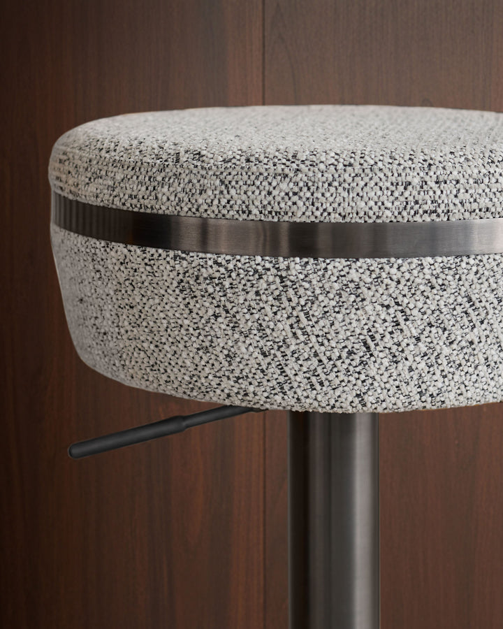 Kian grey fabric bar stool with metal band detail and black footrest, side view against wood paneling.