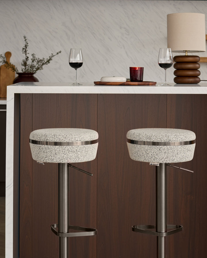 Kian gas lift bar stools with grey textured fabric seats, stainless steel bases, and metal footrests positioned at a kitchen counter.