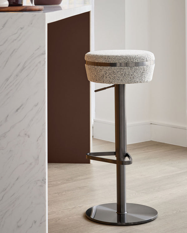 Kian grey fabric gas lift bar stool with dark metal base and footrest, shown in modern kitchen setting.